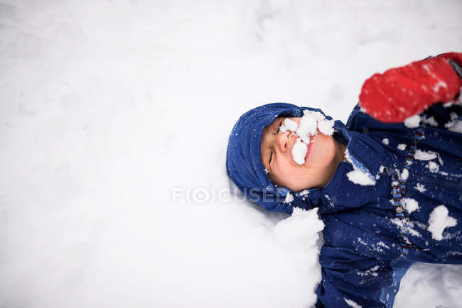 Ragazzo felice sdraiato a terra coperto di neve, USA — Foto stock