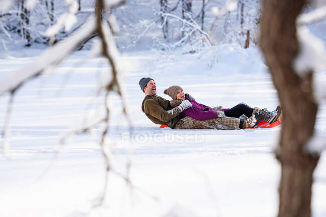 Hombre y mujer bajando en trineo por una colina en la nieve, EE.UU. - foto de stock