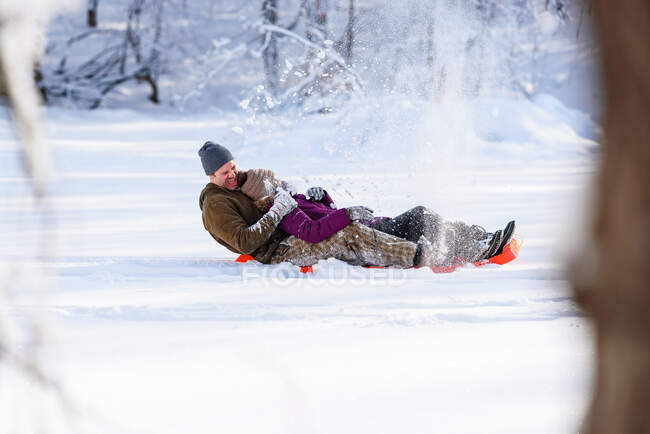 Hombre y mujer bajando en trineo por una colina en la nieve, EE.UU. - foto de stock