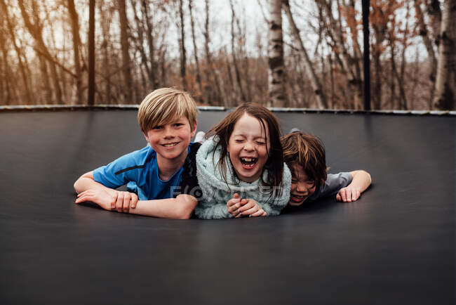 Трое улыбающихся детей лежат на батуте в саду, США — стоковое фото