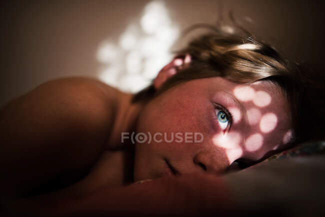 Menino deitado na cama com luz solar no rosto — Fotografia de Stock
