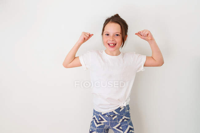 Girl standing by a wall flexing her muscles — Stock Photo