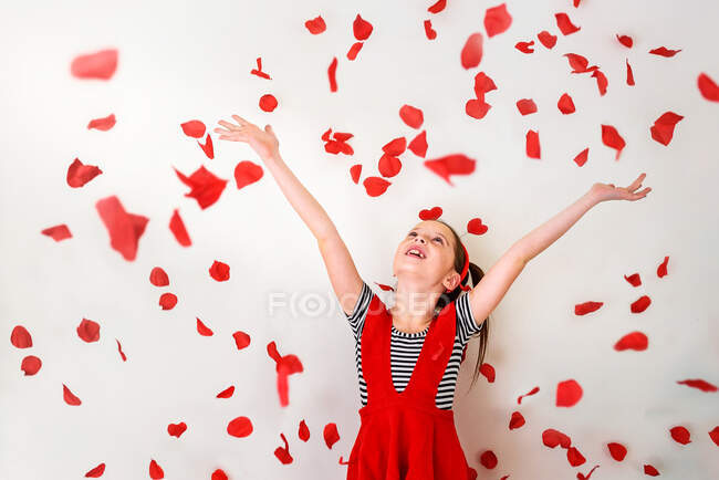 Happy girl throwing red flower petals in the air — Stock Photo