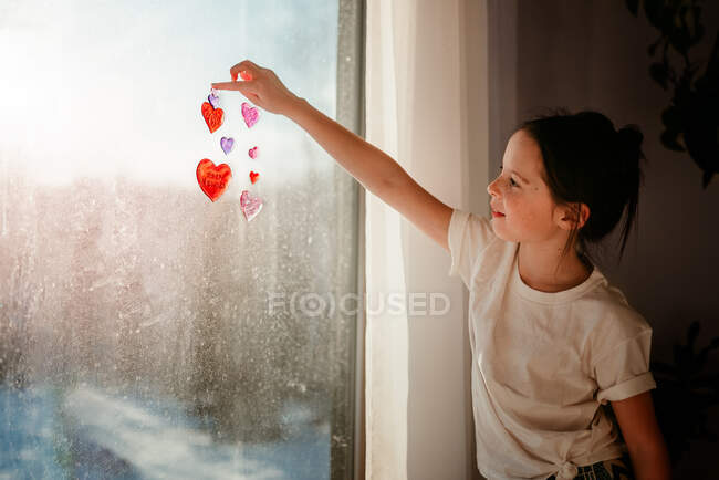 Girl sticking heart decorations on a window — Stock Photo