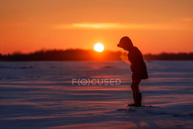 Silhouette eines Mädchens, das bei Sonnenuntergang in einem verschneiten Feld steht, USA — Stockfoto