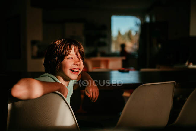 Joyeux garçon assis à une table de salle à manger — Photo de stock