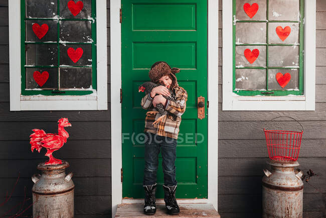 Menino em pé na frente de um galinheiro abraçando uma galinha, EUA — Fotografia de Stock