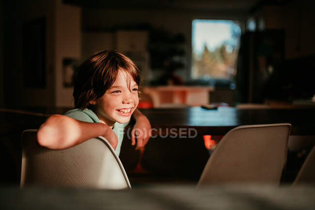 Niño feliz sentado en una mesa de comedor - foto de stock