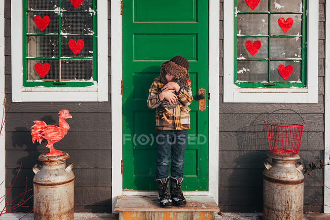 Boy standing in front of a chicken coop hugging a chicken, USA — Stock Photo