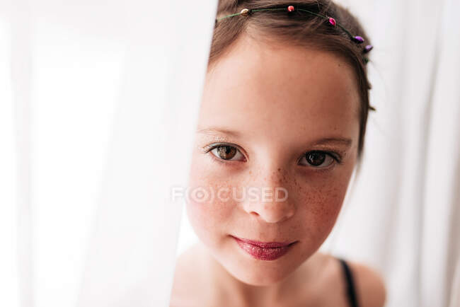 Portrait of a young girl wearing make-up standing by a curtain — Stock Photo