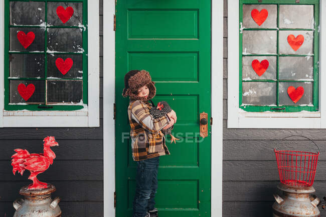 Мальчик, стоящий перед курятником, обнимающий курицу, США — стоковое фото