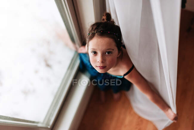Vista aérea de una niña de pie junto a una ventana - foto de stock