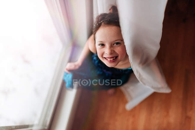 Портрет молодой девушки, стоящей у окна, держа занавес — стоковое фото
