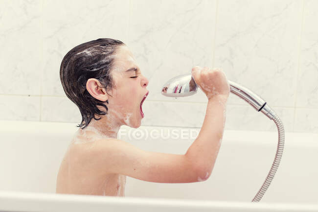Boy sitting in bath singing into a shower head — Stock Photo
