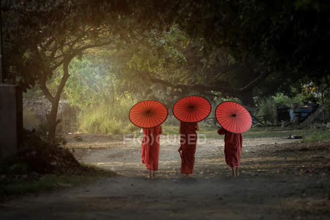 Tres monjes novicios caminando por un camino, Bagan, Mandalay, Myanmar - foto de stock