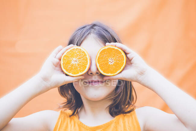 Portrait of a boy with long hair holding halved oranges in front of his eyes — Stock Photo