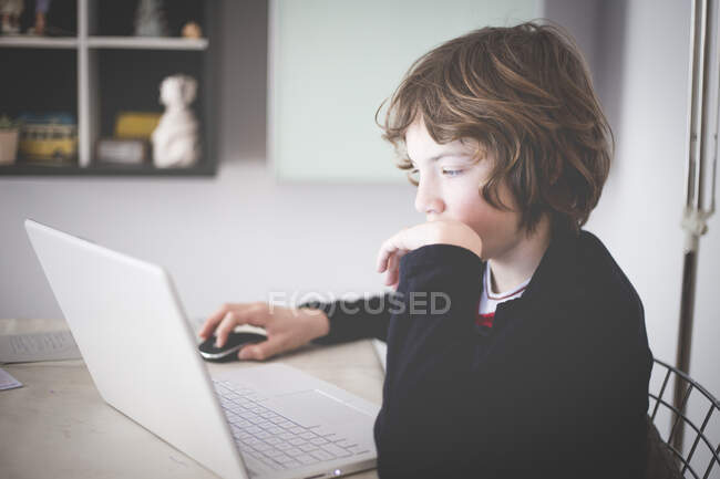 Chico sentado en una mesa haciendo su tarea - foto de stock