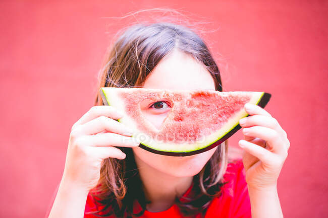 Boy with long hair looking through a heart shape in a piece of watermelon — Stock Photo