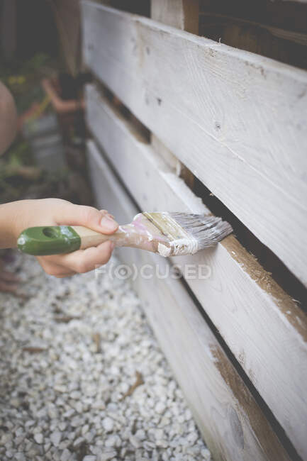 Boy painting a wooden fence in the garden — Stock Photo