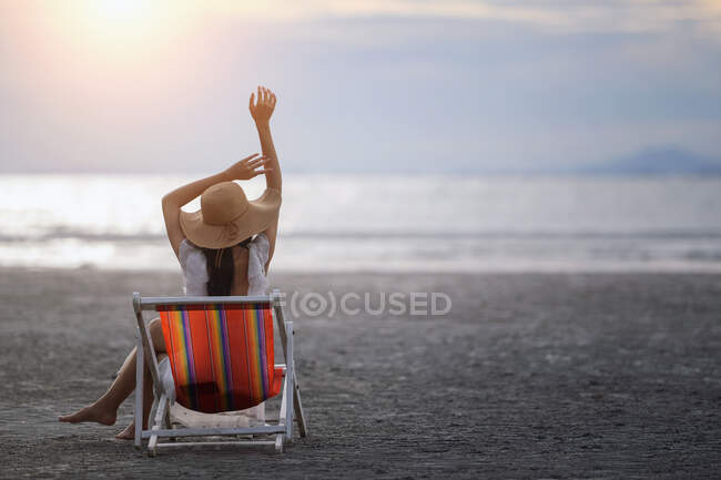 Вид сзади на женщину, сидящую в шезлонге на пляже на закате, Таиланд — стоковое фото