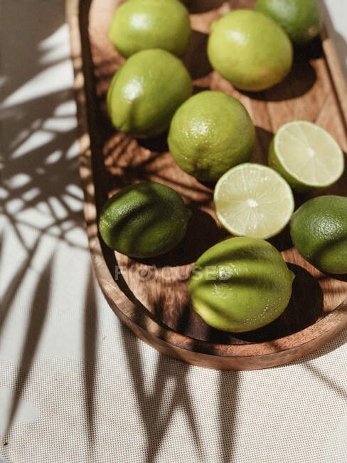 Fresh limes on a wooden tray in the shadows — Stock Photo
