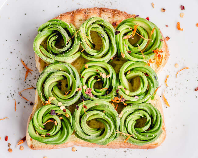 Toast with avocado roses, chilli flakes and edible flowers — Stock Photo