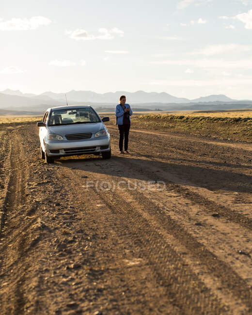 Woman standing next to a broken down car talking on phone, Wyoming, USA — Stock Photo