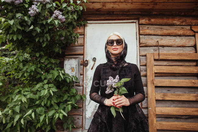 Schöne Frau mit einer Fliederblume vor einem Gebäude — Stockfoto