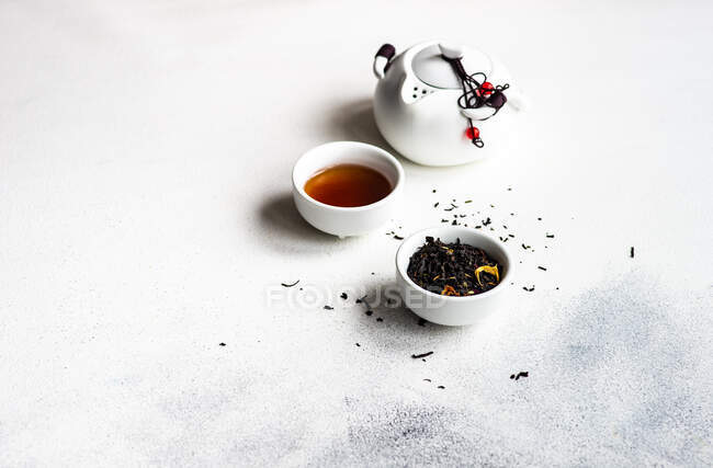 Taza de té con hojas de té y una tetera - foto de stock
