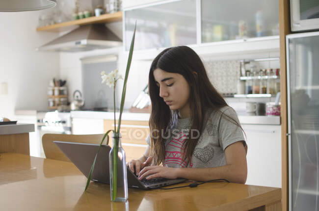 Дівчина-підліток сидить на кухні за допомогою ноутбука — стокове фото