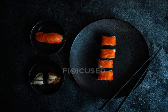 Набор суши с рулонами филаделии подается на каменном столе с палочками для еды — стоковое фото
