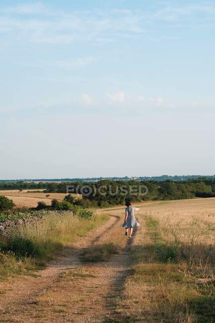 Rear view of a woman running along a country road, France — Stock Photo