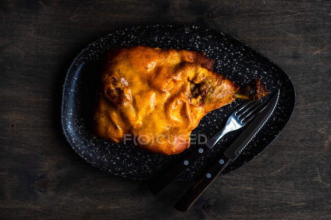Vista aérea de una pata de cerdo asada tradicional en un plato de servir con cubiertos - foto de stock