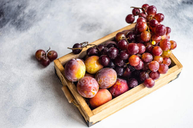 Дерев'яний лоток, наповнений сливами та виноградом — стокове фото