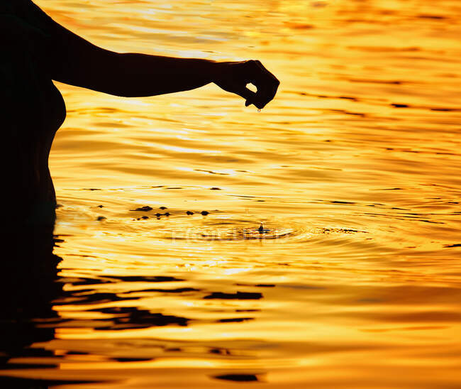 Silhouette einer Frau, die bei Sonnenuntergang mit ausgestrecktem Arm im Meer steht, Malta — Stockfoto