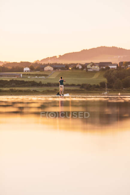 Jovem mulher levante-se paddleboarding ao pôr do sol, Lago Wallersee, Flachgau, Salzburgo, Áustria — Fotografia de Stock