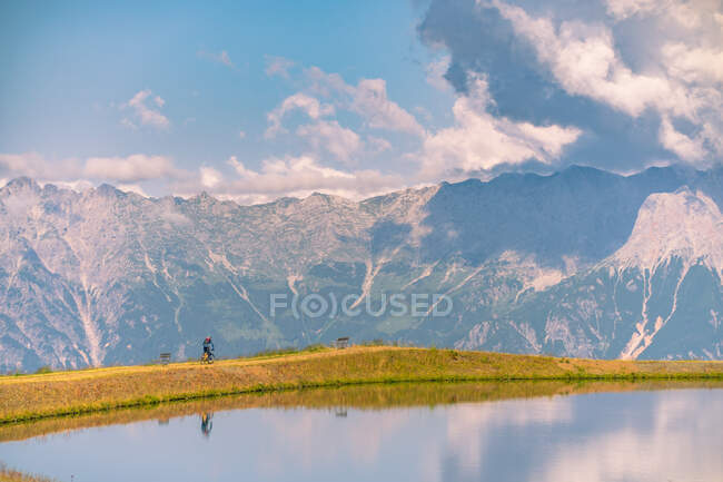 Homme passant à vélo devant un lac dans les Alpes autrichiennes, Saalbach, Zell am See, Salzbourg, Autriche — Photo de stock