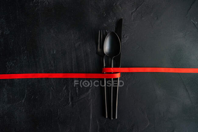 Красная лента, связанная вокруг столовых приборов на черном фоне — стоковое фото