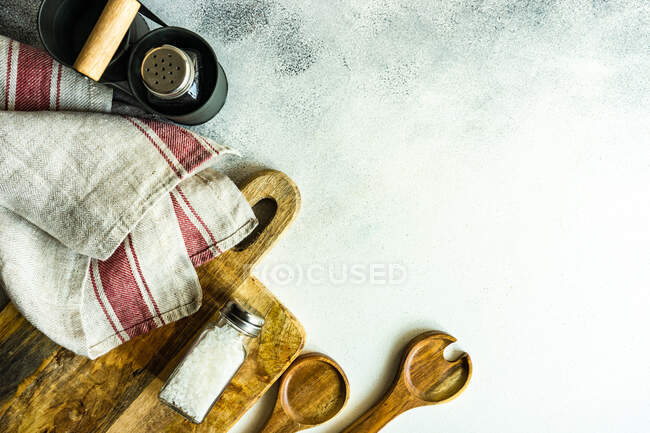 Ollas de sal y pimienta en una mesa con una toalla de té, tabla de cortar y cucharas de servir - foto de stock