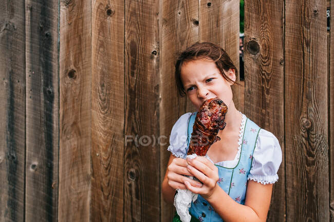 Ragazza in piedi vicino a una recinzione che mangia una coscia di tacchino alla griglia, USA — Foto stock