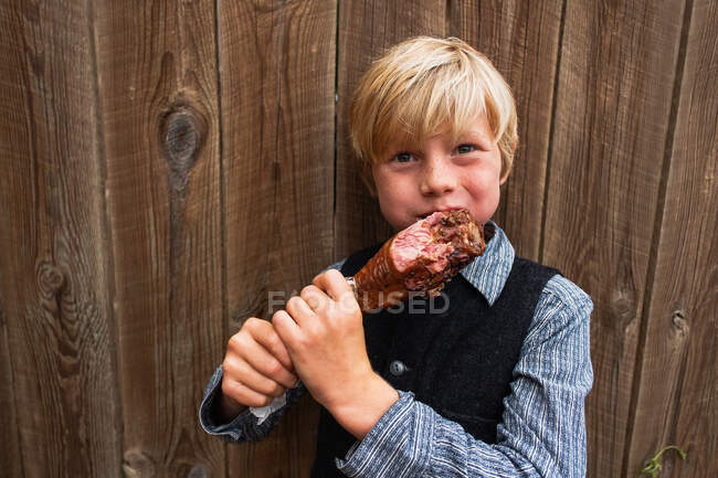 Ragazzo in piedi vicino a una recinzione che mangia una coscia di tacchino alla griglia, USA — Foto stock