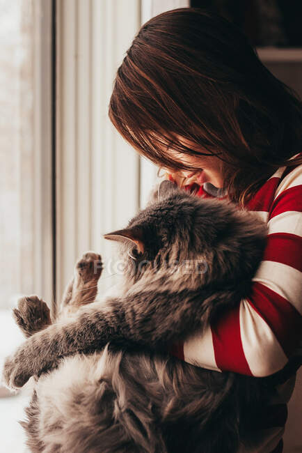 Lächelndes Mädchen steht am Fenster und kuschelt ihre Katze — Stockfoto