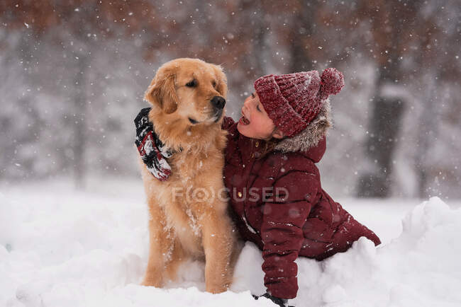 Menina sentada na neve abraçando seu cão golden retriever, Wisconsin, EUA — Fotografia de Stock