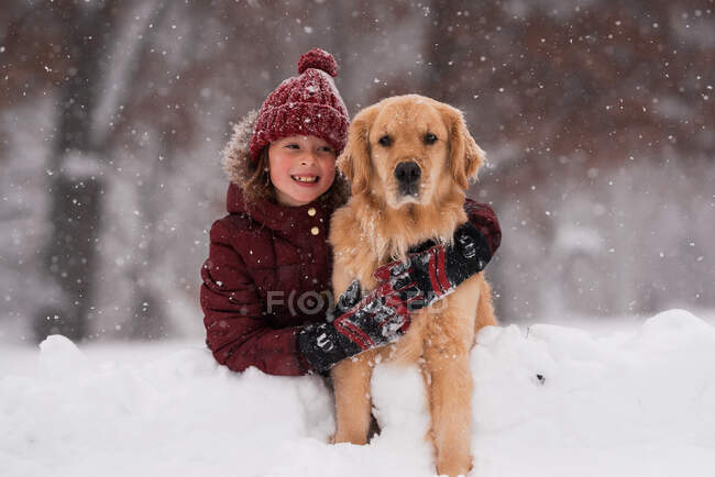 Fille assise dans la neige câlinant son chien golden retriever, Wisconsin, USA — Photo de stock