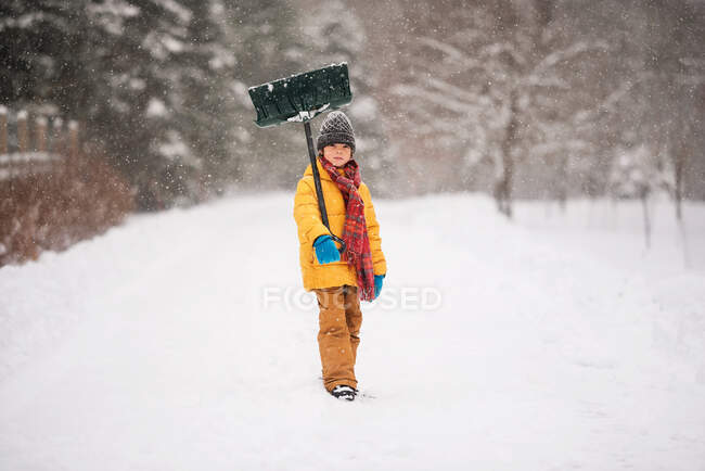 Ragazzo con una pala in piedi sulla neve su un lungo vialetto innevato, Wisconsin, USA — Foto stock
