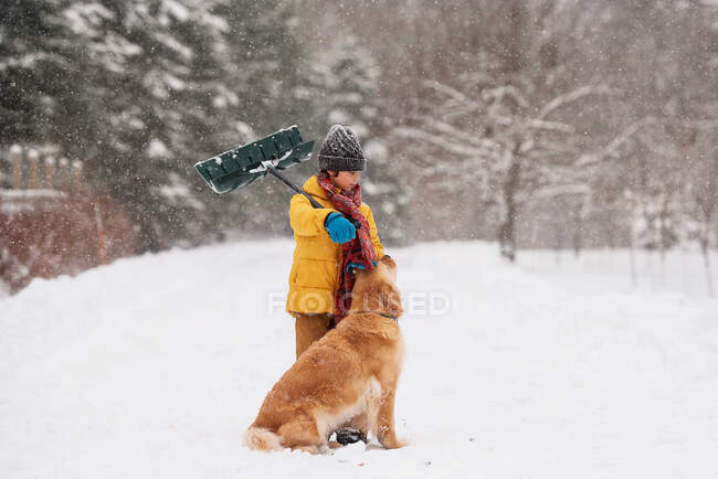 Мальчик с лопатой, стоящий со своей собакой в снегу на длинной снежной дороге, Висконсин, США — стоковое фото