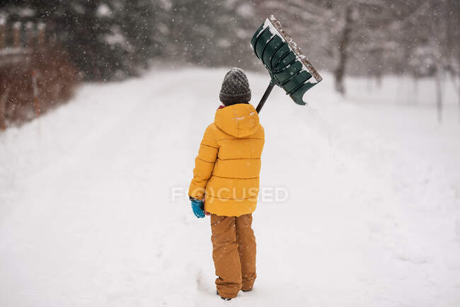 Мальчик с лопатой, стоящей в снегу на длинной снежной дорожке, Висконсин, США — стоковое фото