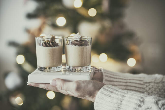 Mujer de pie frente a un árbol de Navidad celebración de chocolate turrón crema de mantequilla petit fours - foto de stock