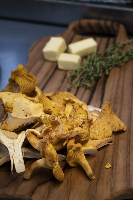 Wild mushrooms on a chopping board with butter and thyme — Stock Photo