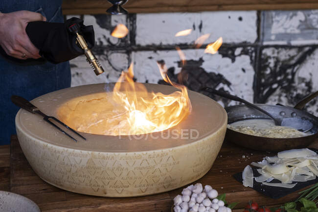 Homem aquecendo o interior de um queijo grana padano inteiro com um maçarico — Fotografia de Stock